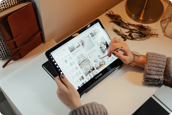 Top view of a person sitting at wooden desk planning budget on tablet, with stationery and decorative items around.